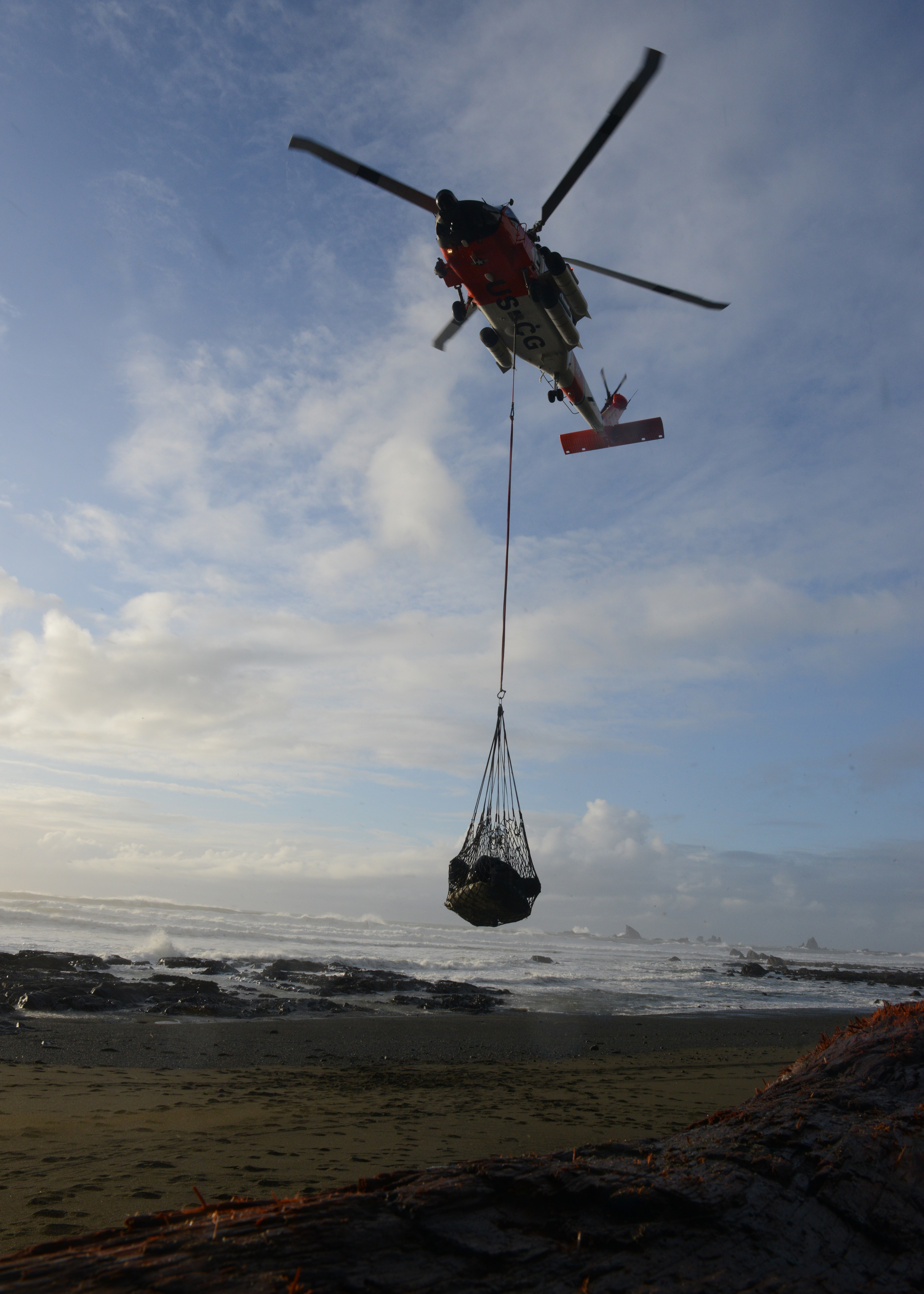 A Coast Guard MH-60 Jayhawk helicopter crew lifting a net full of beach debris