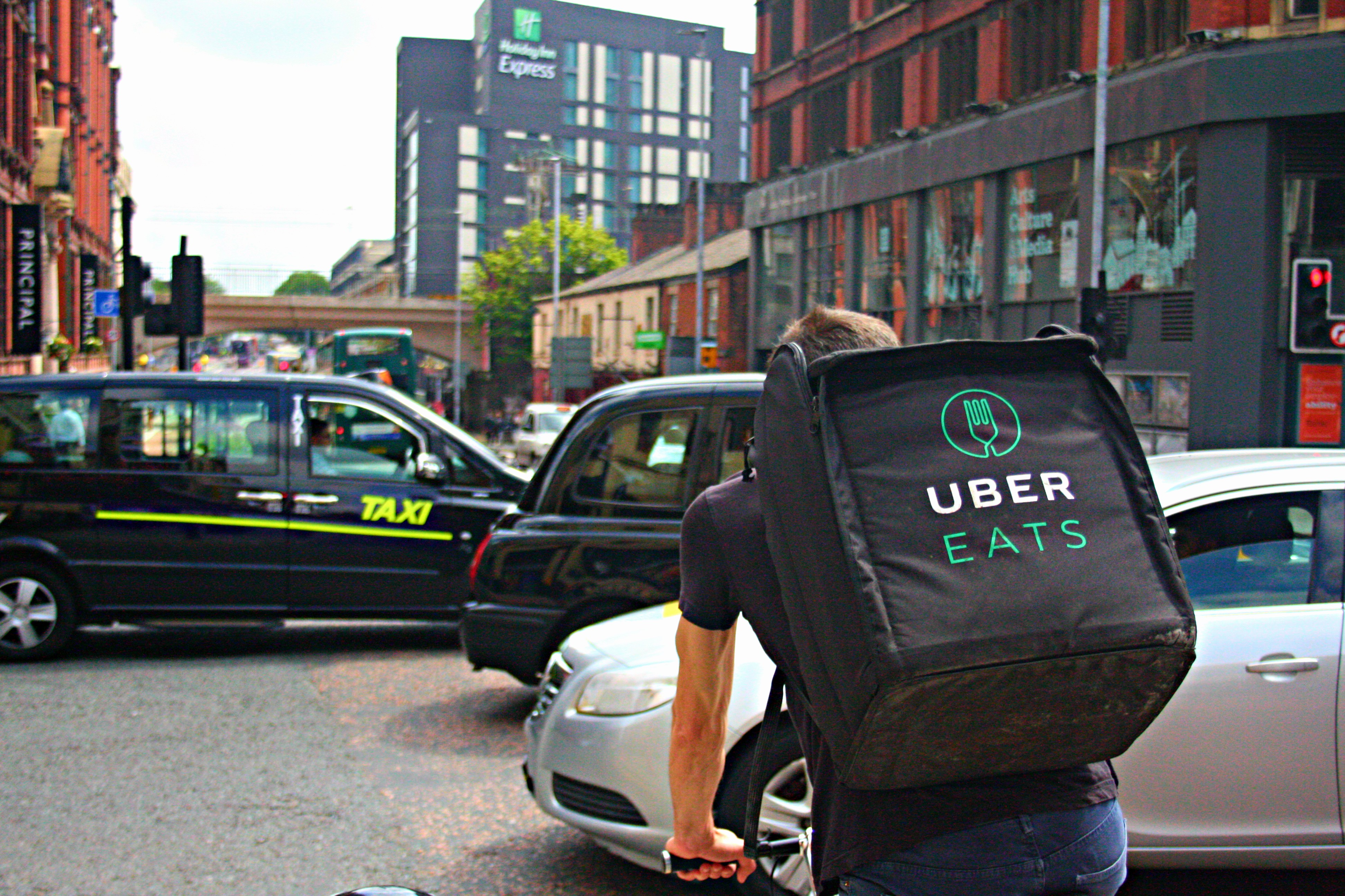 Ciclofattorino di UBER Eats che percorre la trafficata Oxford Road a Manchester