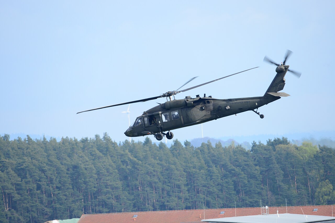 A UH-60 Black Hawk utility helicopter in flight over a military airfield.