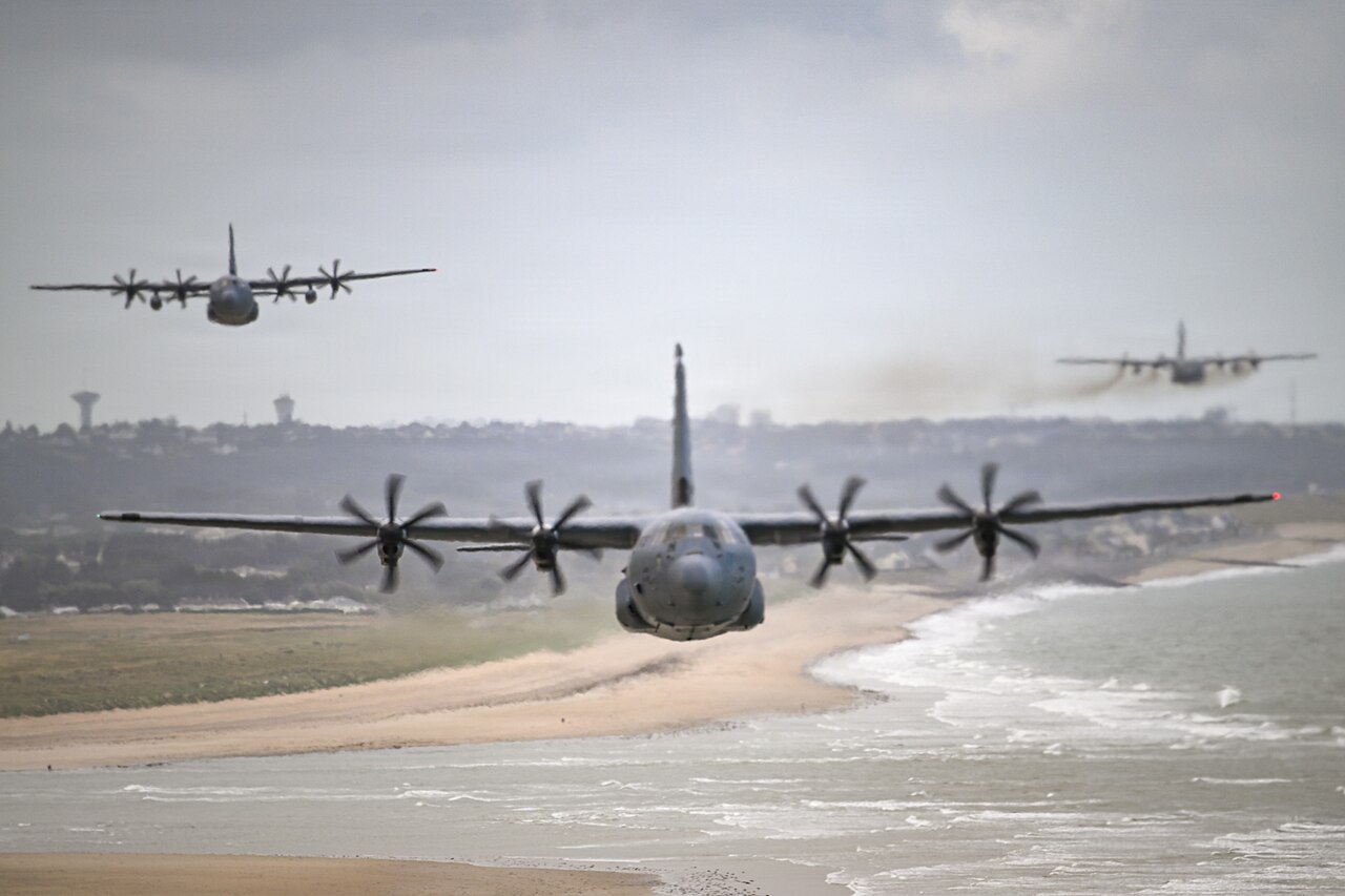 C-130 Hercules military transport aircraft fly in formation over the coast.