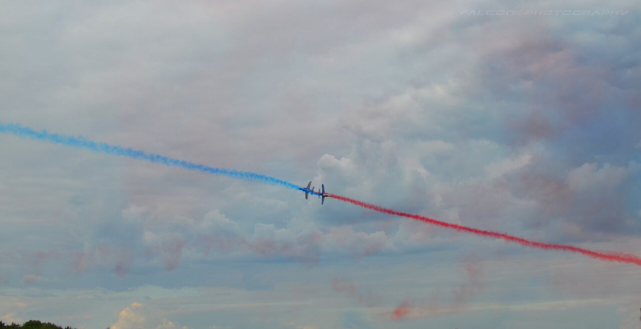 Jets of the Patrouille de France cross in flight trailing coloured smoke.