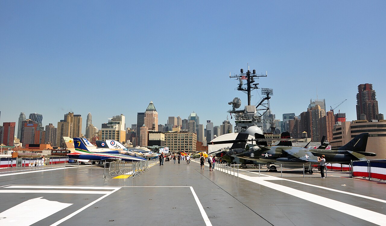 The flight deck of an aircraft carrier lined with military aircraft.