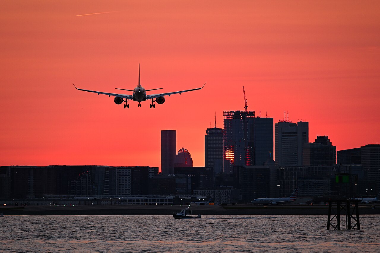 Airliner on final approach over a city at sunset.