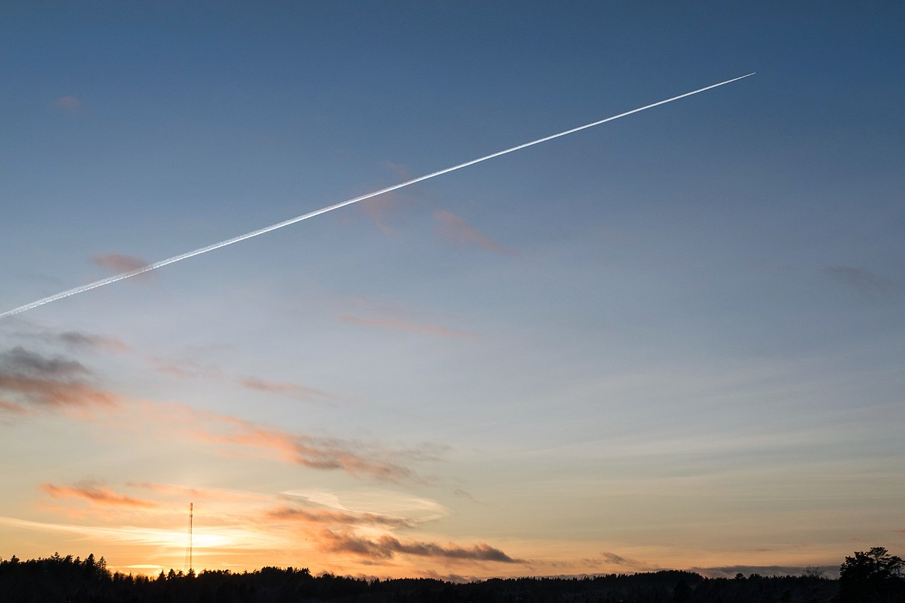 Contrail above a telecommunications mast at sunset.