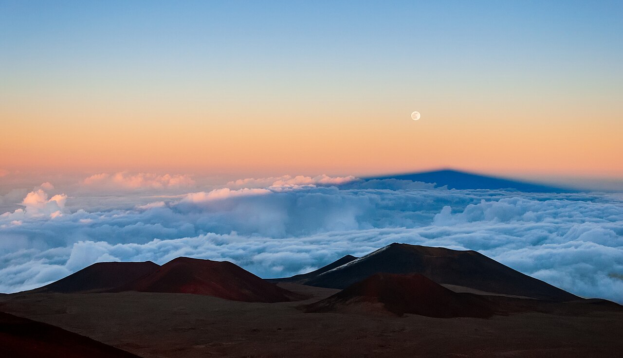 Full moon rising above a sea of clouds from a volcano summit.