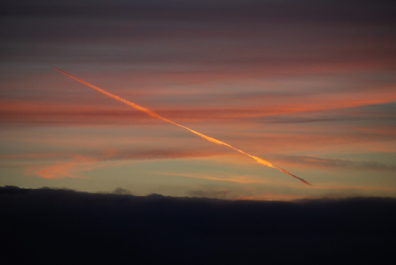 A jet contrail glowing gold in the twilight sky.
