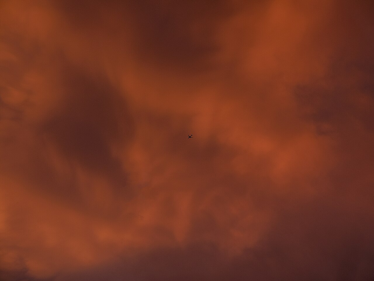 Silhouette of an aircraft against a red storm sky at sunset.