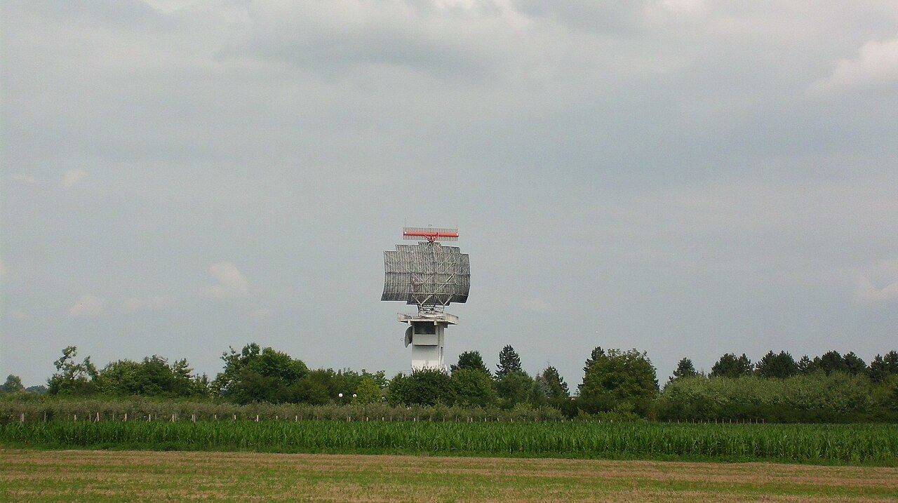 Airport surveillance radar antenna above green fields.